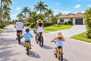 A family riding bicycles on a residential street with palm trees and houses.