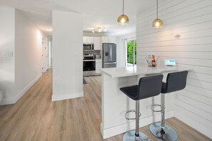 A modern kitchen with white cabinetry, stainless steel appliances, and a central island with bar stools.