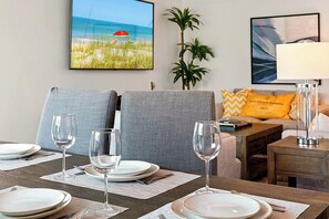 A dining area with a table set for four, two chairs, a lamp, and artwork on the walls.