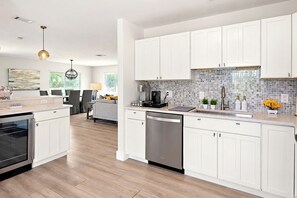 A modern kitchen with white cabinetry, a dishwasher, and a coffee maker. - VillaLux: Heated Saltwater Pool & Spa, Walk to Vanderbilt Beach, Bikes (Naples)