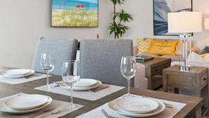 A dining table set with plates, cutlery, and wine glasses, a sofa with cushions, a lamp, and a framed picture of a beach scene.