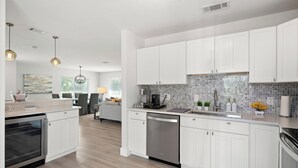 A modern kitchen with white cabinets, a dishwasher, and a tiled backsplash.