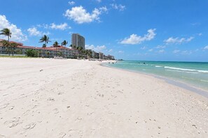 A wide sandy beach with footprints, a clear blue sky, and buildings in the background. - VillaLux: Heated Saltwater Pool & Spa, Walk to Vanderbilt Beach, Bikes (Naples)