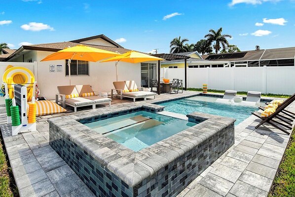 A backyard with a swimming pool, lounge chairs, and umbrellas.