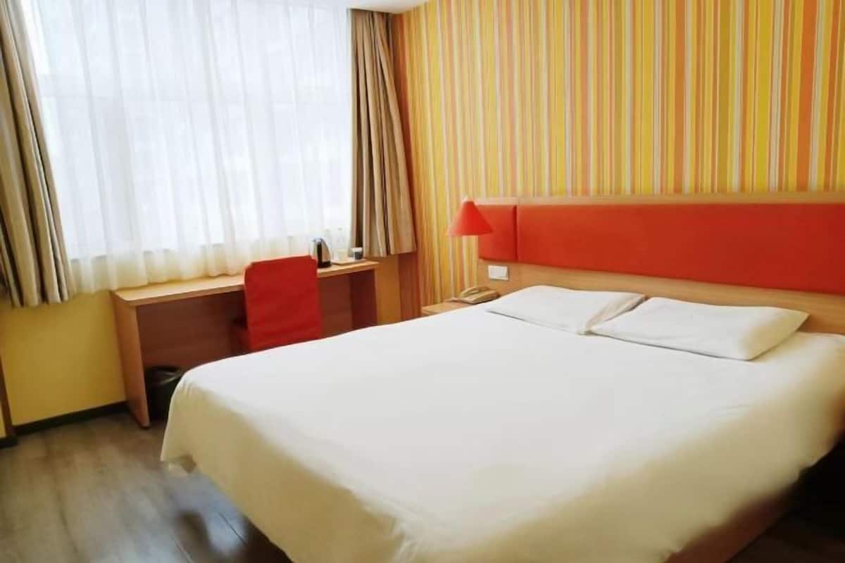 A hotel room with a bed, desk, chair, and a striped wall.