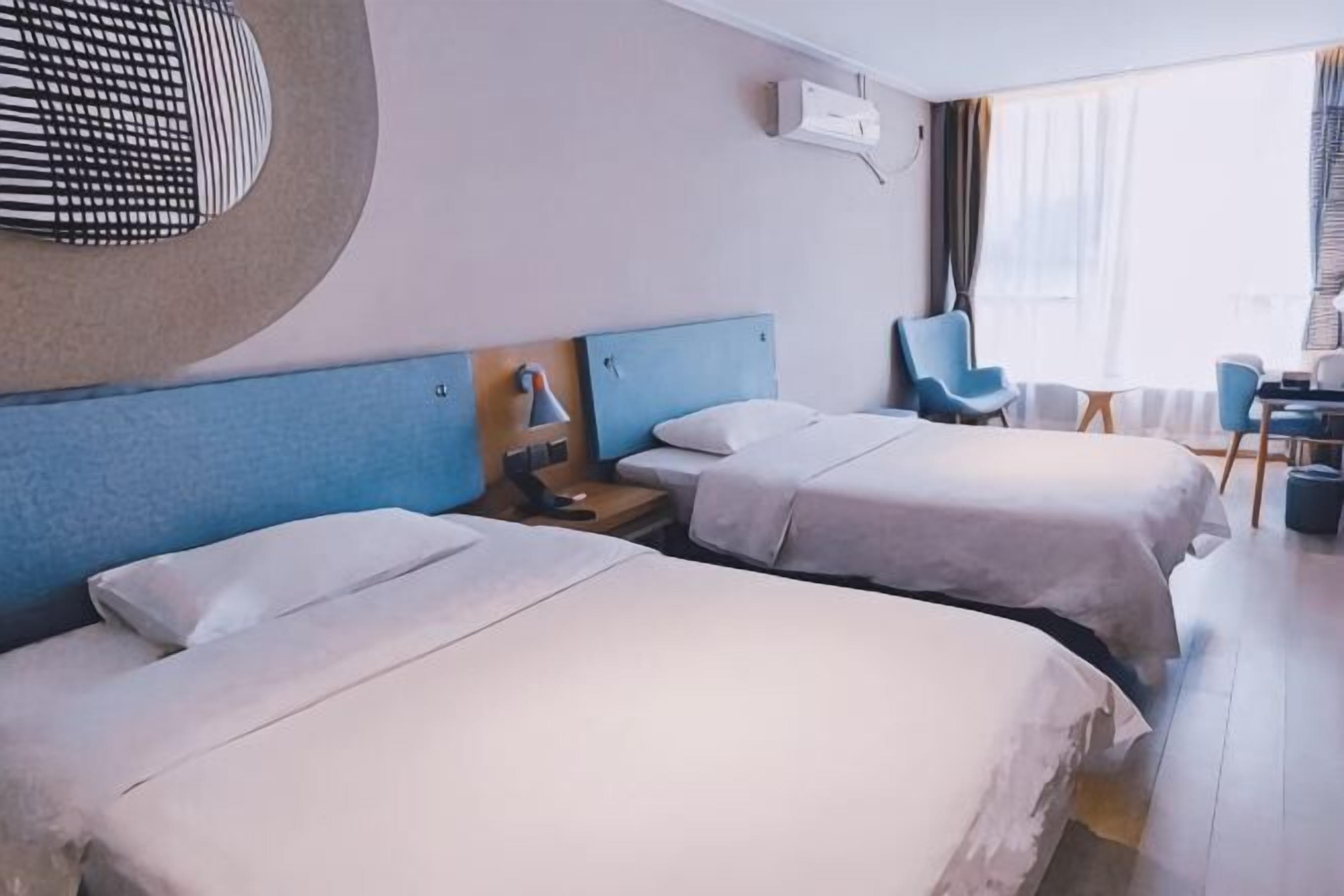 A hotel room with two beds, a desk, a chair, and a view of the outdoors.