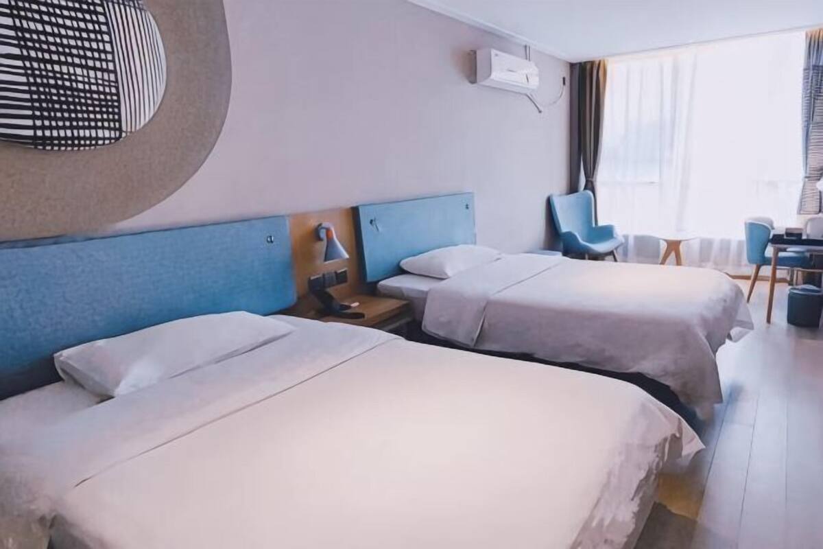 A hotel room with two beds, a desk, a chair, and a view of the outdoors.