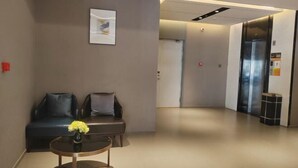 A modern hotel lobby with a reception desk, two sofas, a vase of flowers, and an elevator. - Homeinn Pebble Hotel (Linyi Yinan Government Plaza) (Yinan)