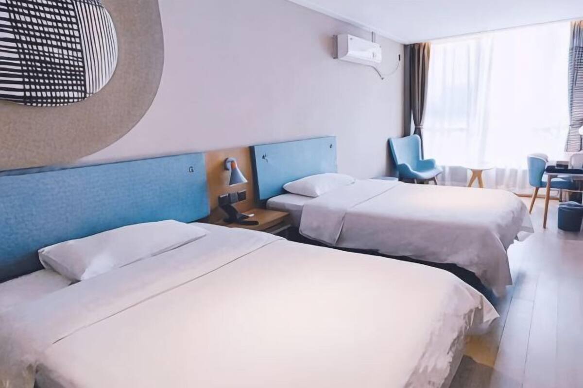 A hotel room with two beds, a desk, a chair, and a window.