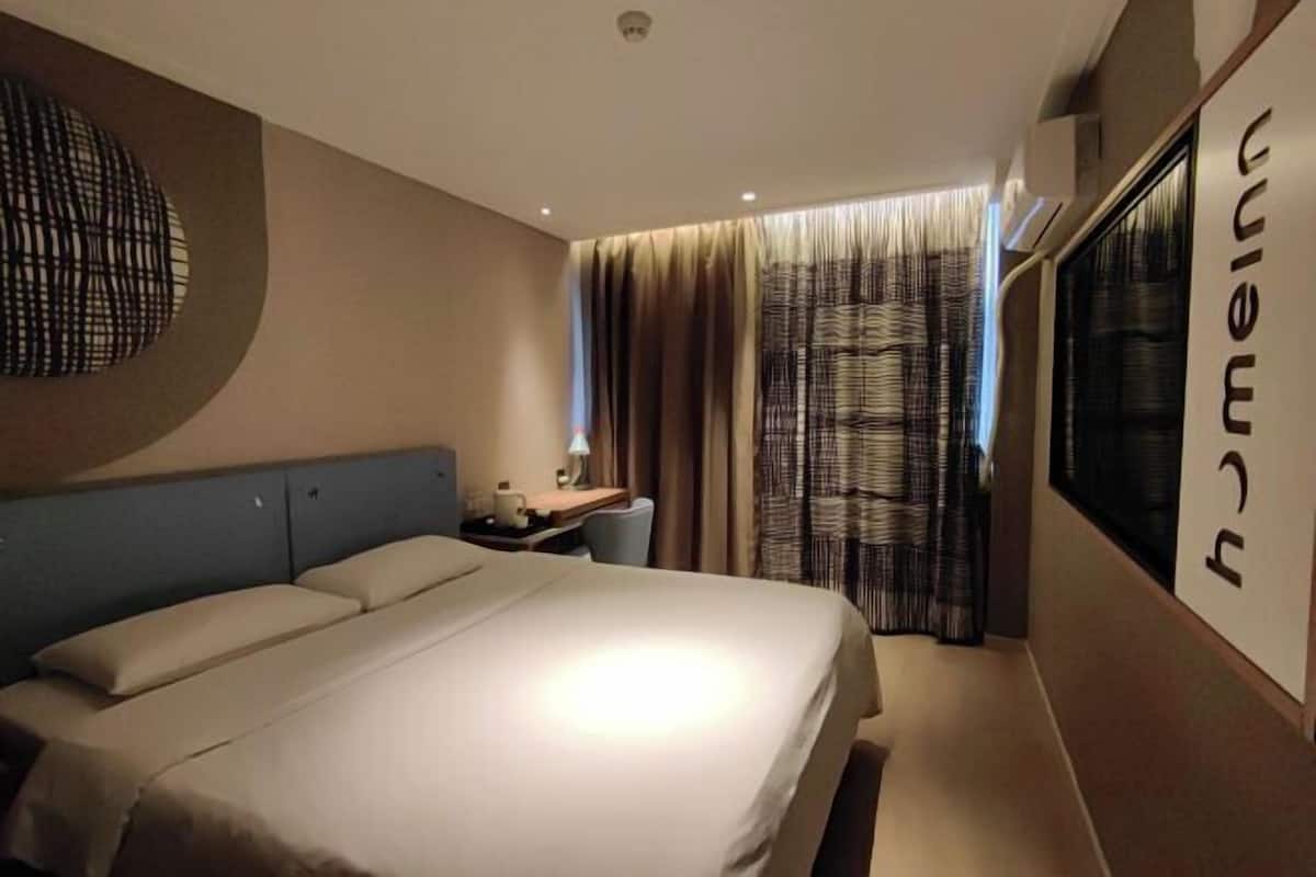 A hotel room with a bed, a desk, a chair, a lamp, and a window with curtains.