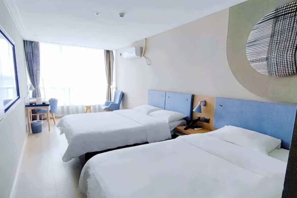 A hotel room with two beds, a desk, a chair, and a large window.