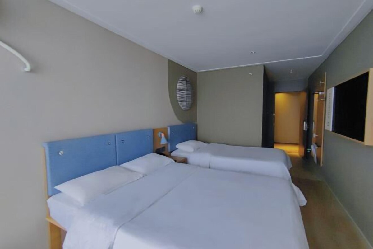 A hotel room with two beds, a TV, and a hallway leading to another room.