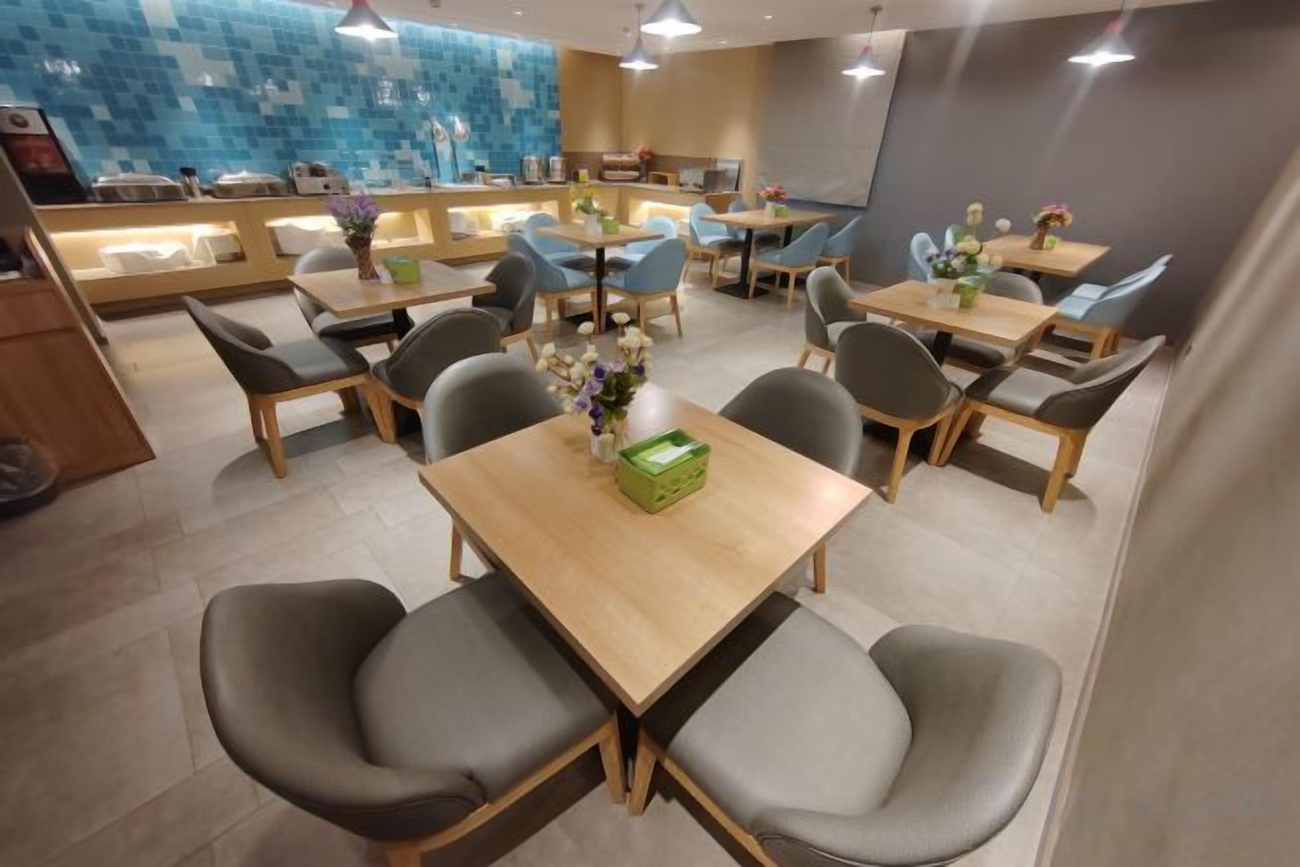 A modern dining area with multiple tables and chairs, a counter with a display case, and a blue-tiled wall in the background.