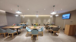 A modern dining area with multiple tables and chairs, recessed ceiling lighting, and a flat-screen TV on the wall. - Homeinn Pebble Hotel (Linyi Yinan Government Plaza) (Yinan)