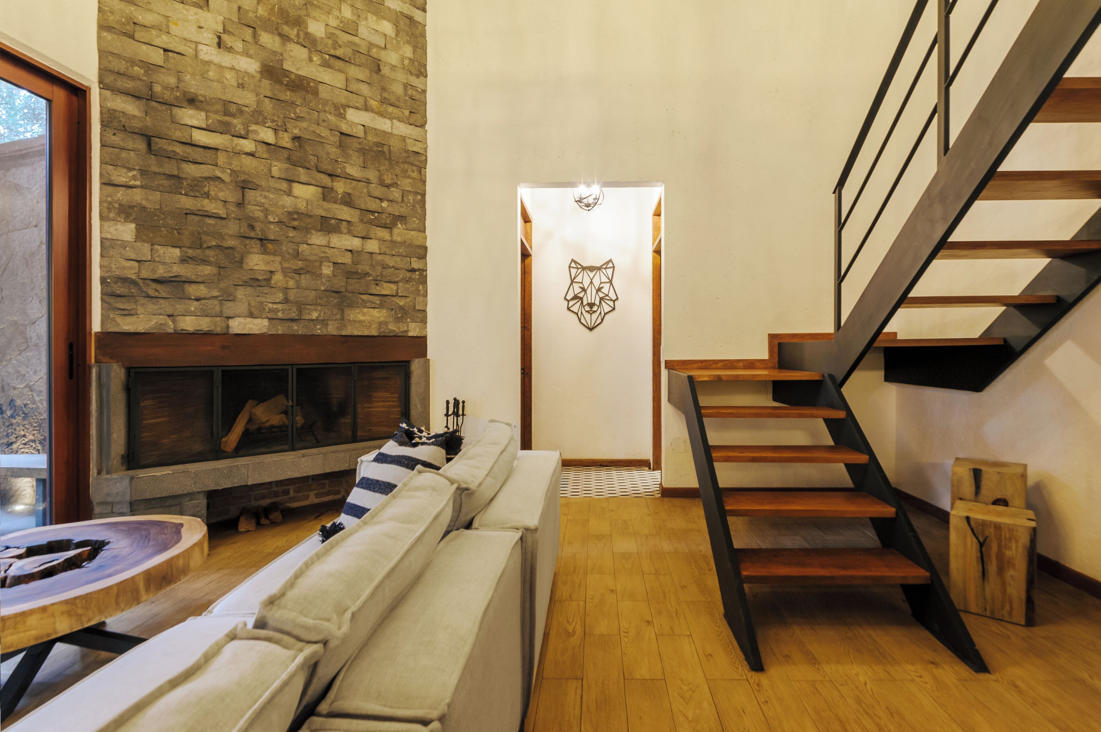 A modern living room with a stone fireplace, a wooden staircase, and a minimalist decor.