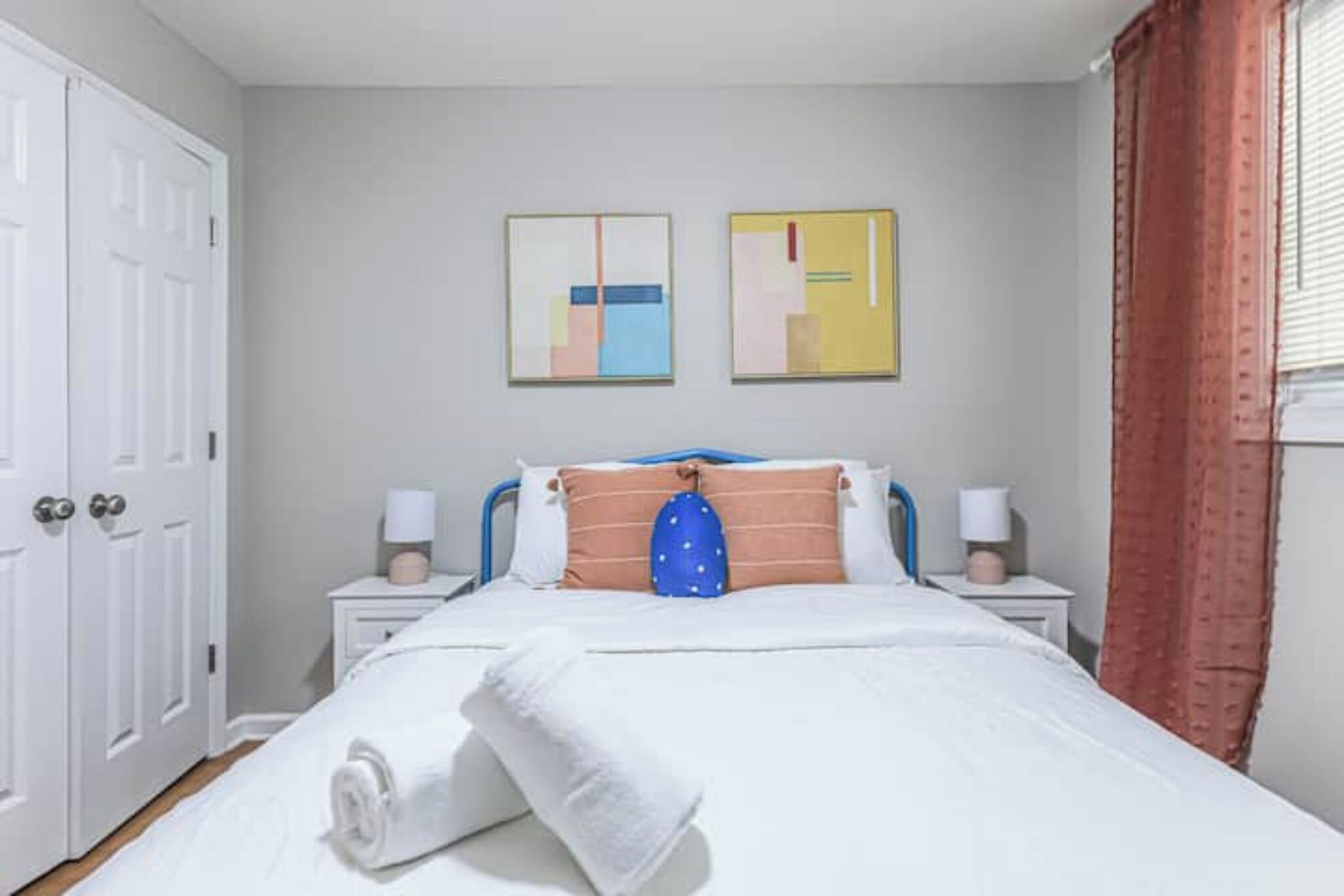 A neatly made bed with white linens, two bedside tables with lamps, and abstract art on the wall.