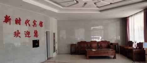 A hotel lobby with a reception desk, a seating area with chairs, and a wall with text.