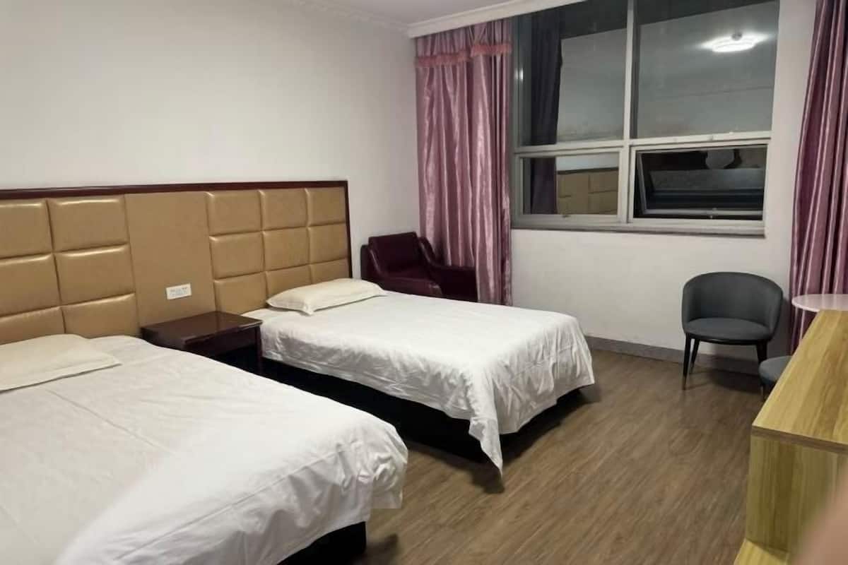 A hotel room with two beds, a desk, a chair, and a window with curtains.