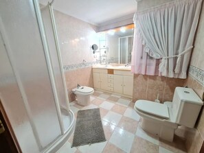 Compact bathroom with shower, toilet, and sink, featuring a checkered tile floor and decorative wall tiles.