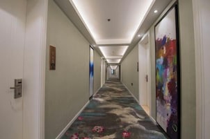 Un pasillo de hotel con alfombra floral, iluminación empotrada y un cuadro abstracto colorido en la pared derecha.
