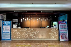 Zona de recepción de hotel con mostrador de mármol, lámparas colgantes y carteles informativos.