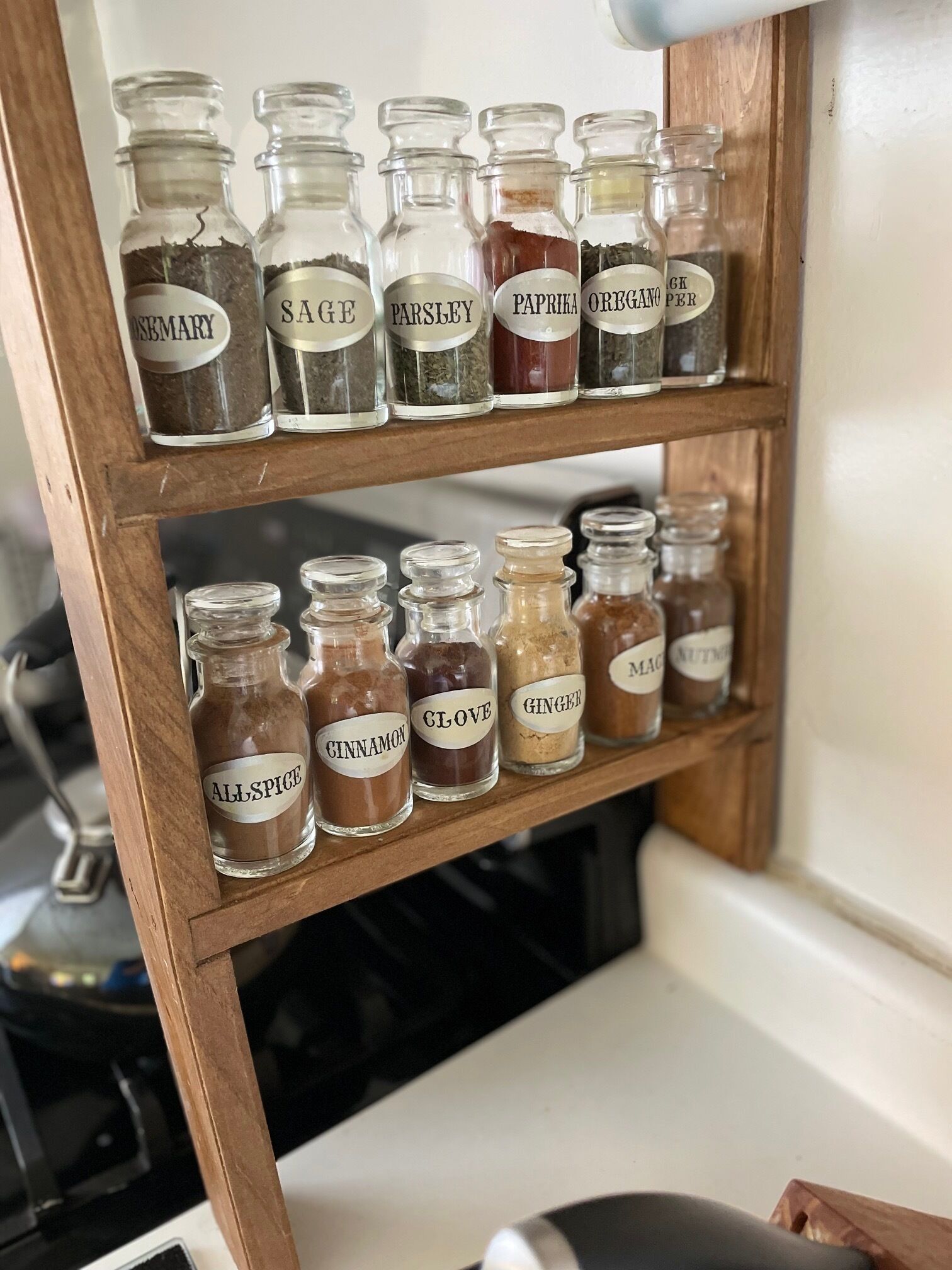 Une étagère en bois sur laquelle sont disposés des bocaux en verre contenant différentes épices.