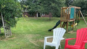 A backyard with a fire pit, two Adirondack chairs, and a wooden play structure. - Charming 3-bedroom cottage in Hampden with AC, WiFi (Hampden)
