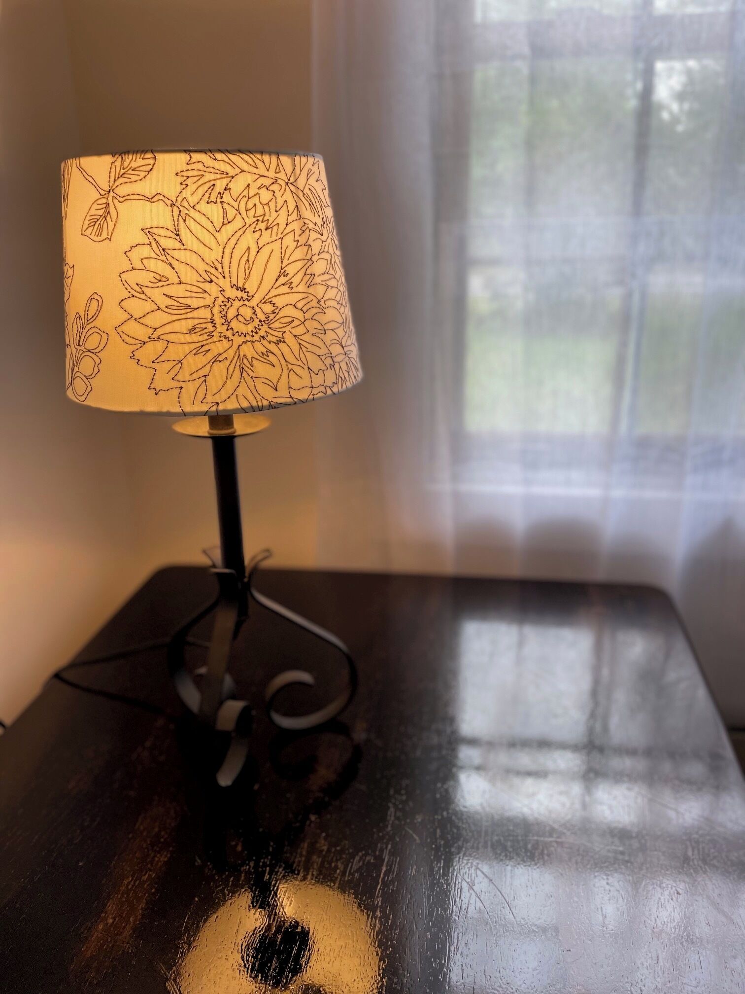 Eine Tischlampe mit floralem Dekor auf einem dunklen Holztisch.
