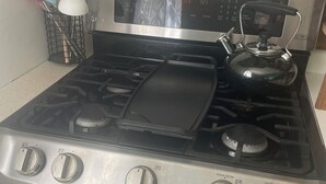 A stainless steel stove with four burners, a kettle, and a digital clock above the stove. - Charming 3-bedroom cottage in Hampden with AC, WiFi (Hampden)