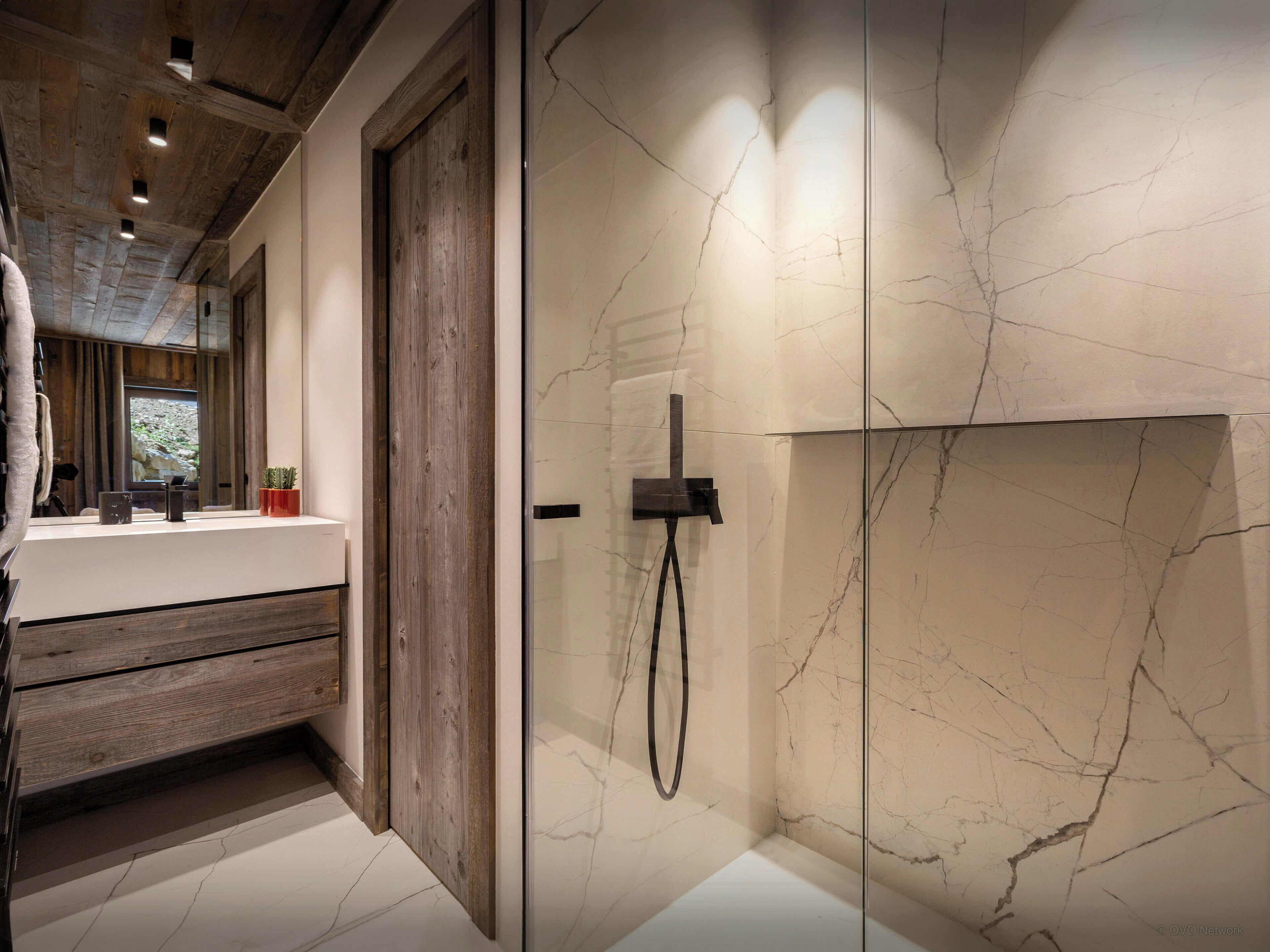 A modern bathroom with a wooden vanity, a glass shower enclosure, and a marble backsplash.