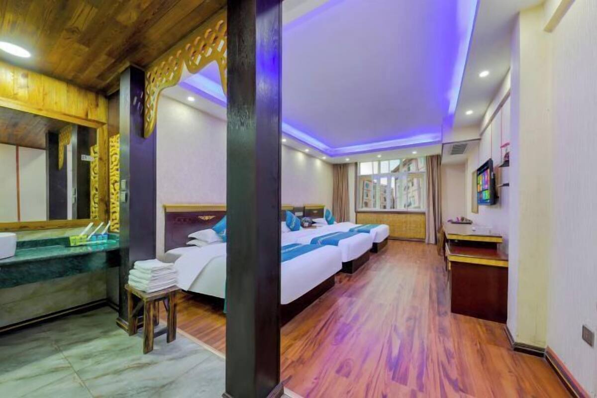 Ein Hotelzimmer mit Holzboden, einem Bett mit blauer Bettwäsche, einem kleinen Tisch und einem Empfangsbereich mit Theke und Stühlen.