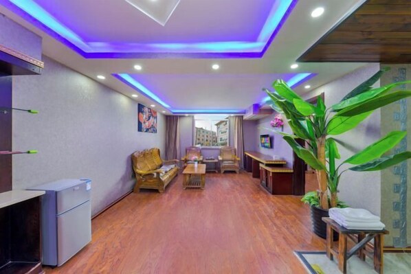 A modern living room with a sofa, coffee table, and chairs. There is a small refrigerator and a potted plant. - Xishuangbanna Peacock Princess Hotel (Jinghong)