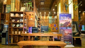 A wooden interior with a reception desk, shelves with various items, and a staircase. - Xishuangbanna Peacock Princess Hotel (Jinghong)
