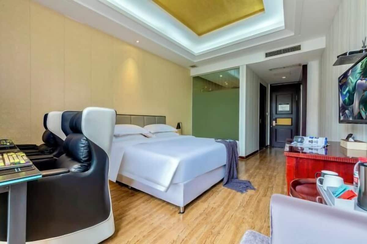 A modern hotel room with a bed, massage chair, desk with computer, and a TV.