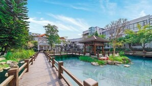 A wooden bridge leading to a pool area with a gazebo and modern buildings in the background. - Chengdu Star Flower Garden Hotel (University Games Sports Center) (Chengdu)