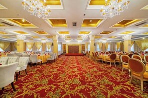 Una sala da banchetto con file di tavoli e sedie, una moquette rossa e lampadari.