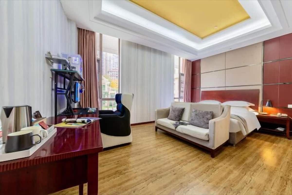 A hotel room with a desk, a sofa, a chair, a bed, and a window with curtains.