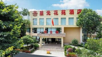 A hotel with a prominent entrance, a flag, and a well-maintained garden area.