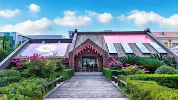 Entrada de hotel con un arco de madera, un camino empedrado y un jardín con diversas plantas y flores.