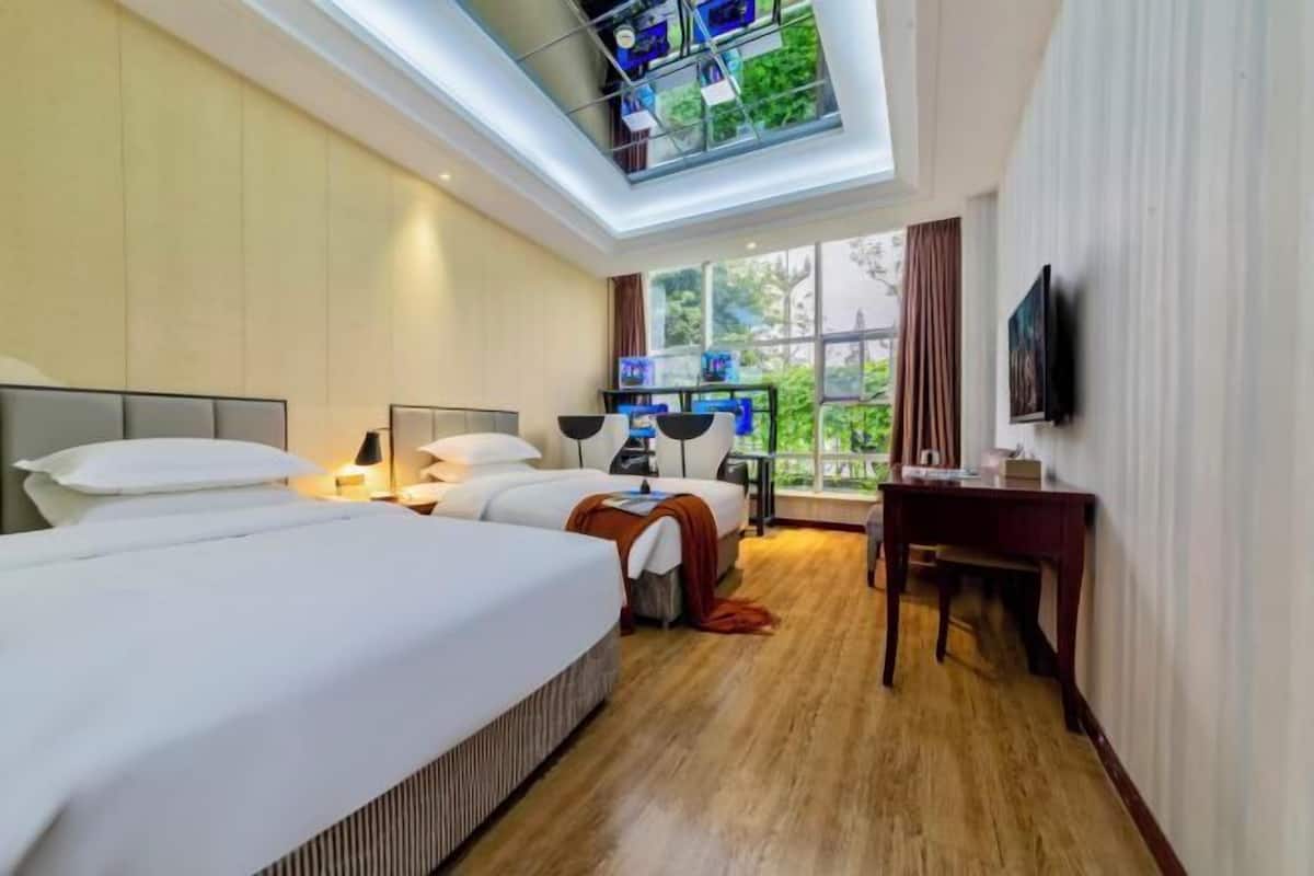 A hotel room with two beds, a desk, a TV, and a skylight.