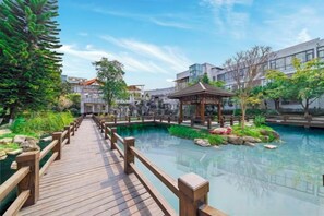 A wooden bridge over a clear pool with a pavilion, surrounded by greenery and buildings. - Chengdu Star Flower Garden Hotel (University Games Sports Center) (Chengdu)
