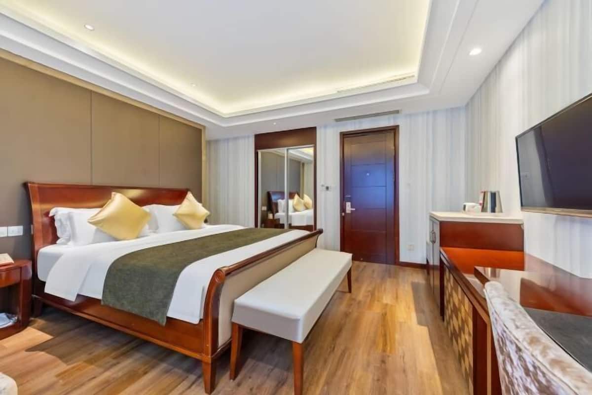 A modern hotel room with a large bed, a bench, a TV, and a mirror.