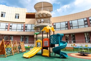 A playground with slides and climbing structures in front of a building with multiple windows and a balcony. - Chengdu Star Flower Garden Hotel (University Games Sports Center) (Chengdu)