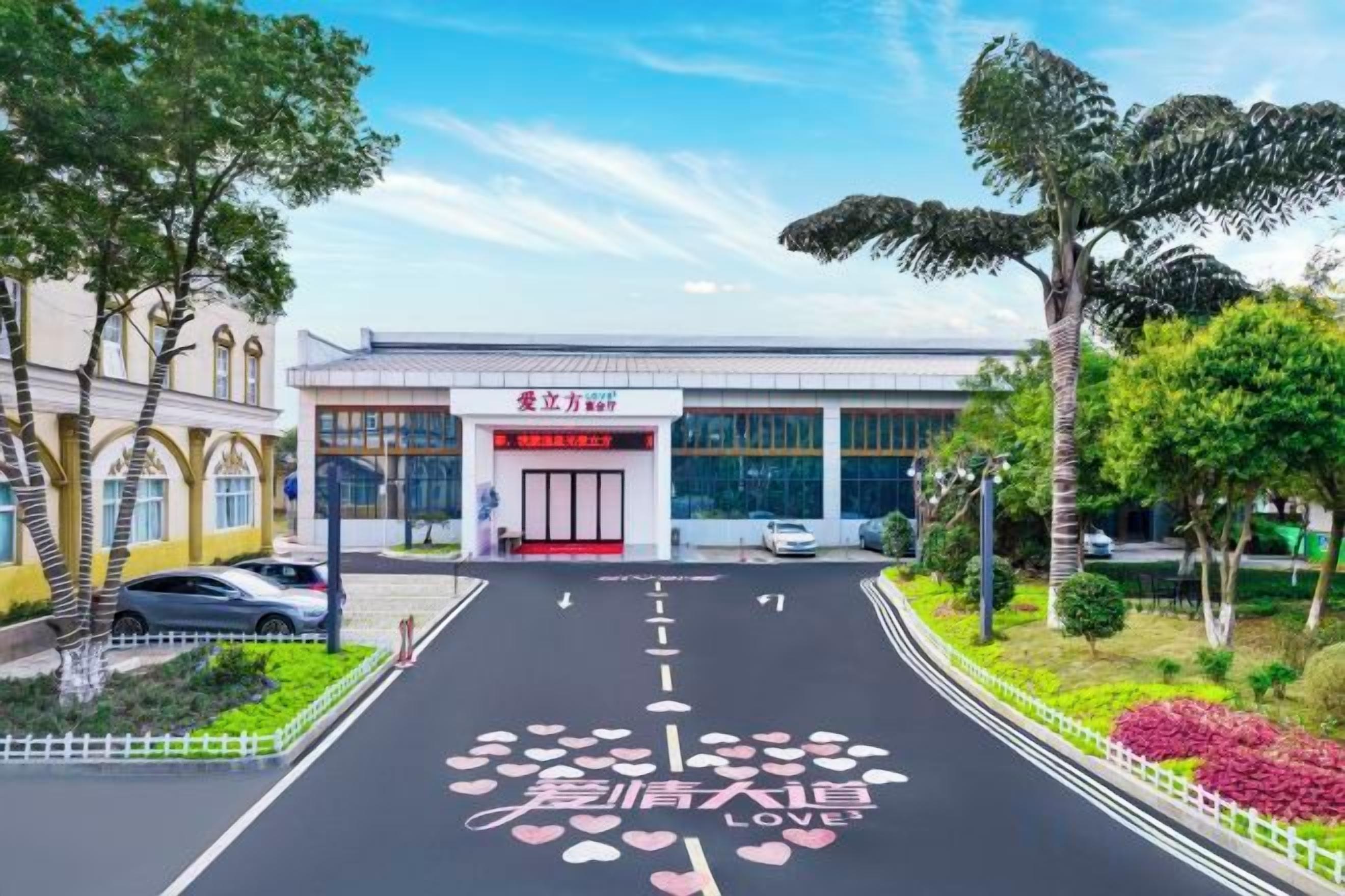 Un edificio con un letrero de entrada rojo, un estacionamiento y una carretera con marcas en forma de corazón.