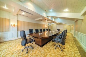 Un salón de conferencias con una larga mesa, múltiples sillas y piso alfombrado.