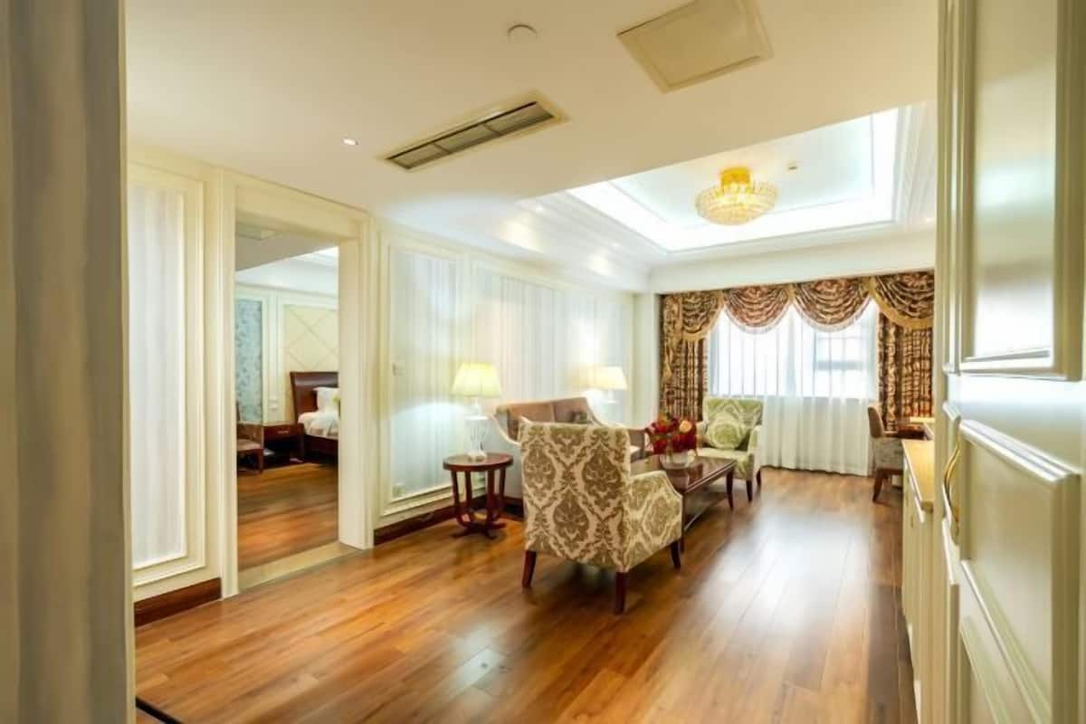 A spacious living room with a high ceiling, a chandelier, and a view through a large window.