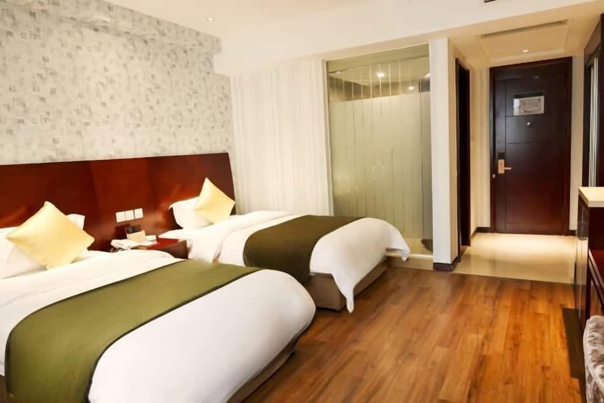 A hotel room with two beds, a wooden floor, a large window, and a door.