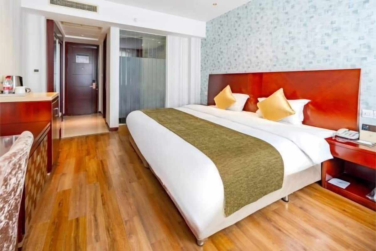 A hotel room with a large bed, a wooden floor, a desk with a telephone, and a door leading to another room.