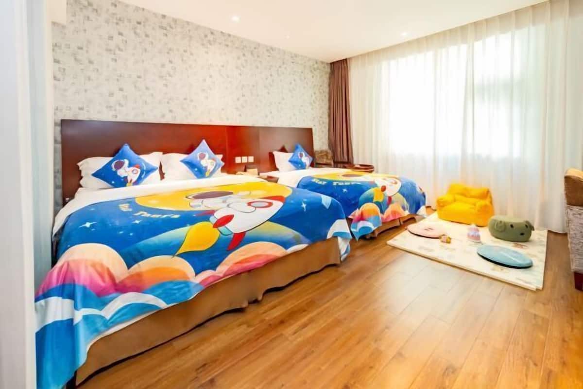 A hotel room with two beds, a wooden floor, a patterned wall, and a window with curtains.