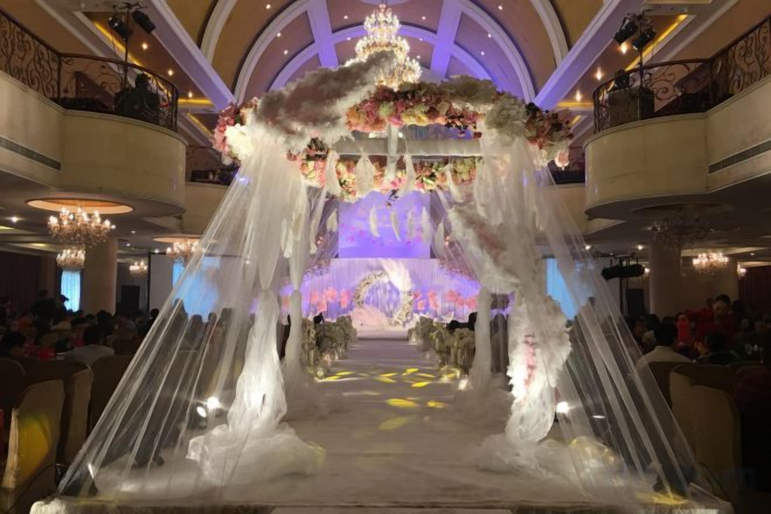 An indoor venue with a central aisle leading to a stage, surrounded by balconies and chandeliers.